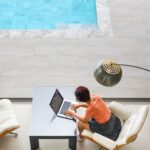 Frau sitzt mit ihrem Laptop am Pool als Symbol für krankenversicherung ausland