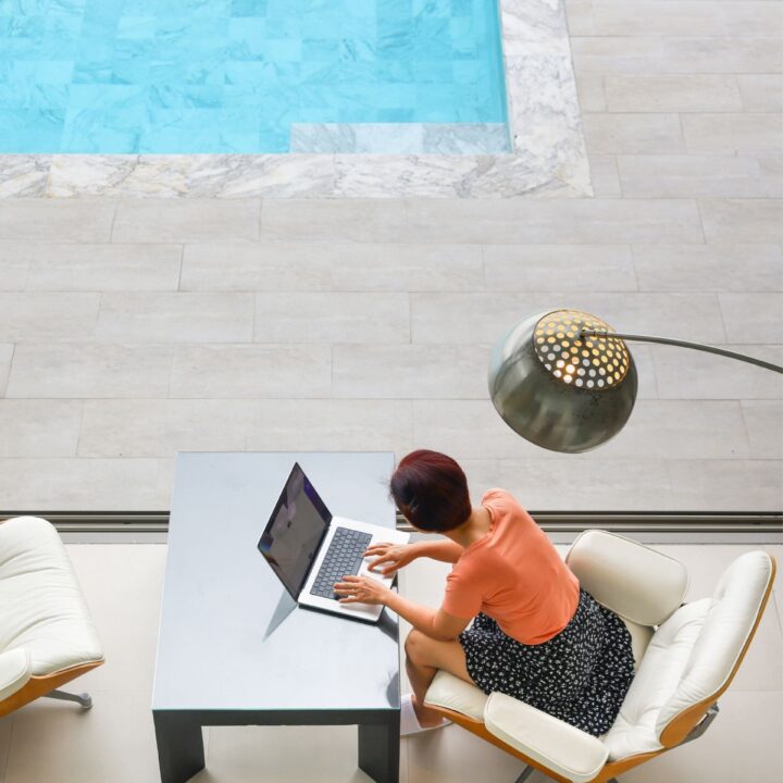 Frau sitzt mit ihrem Laptop am Pool als Symbol für krankenversicherung ausland
