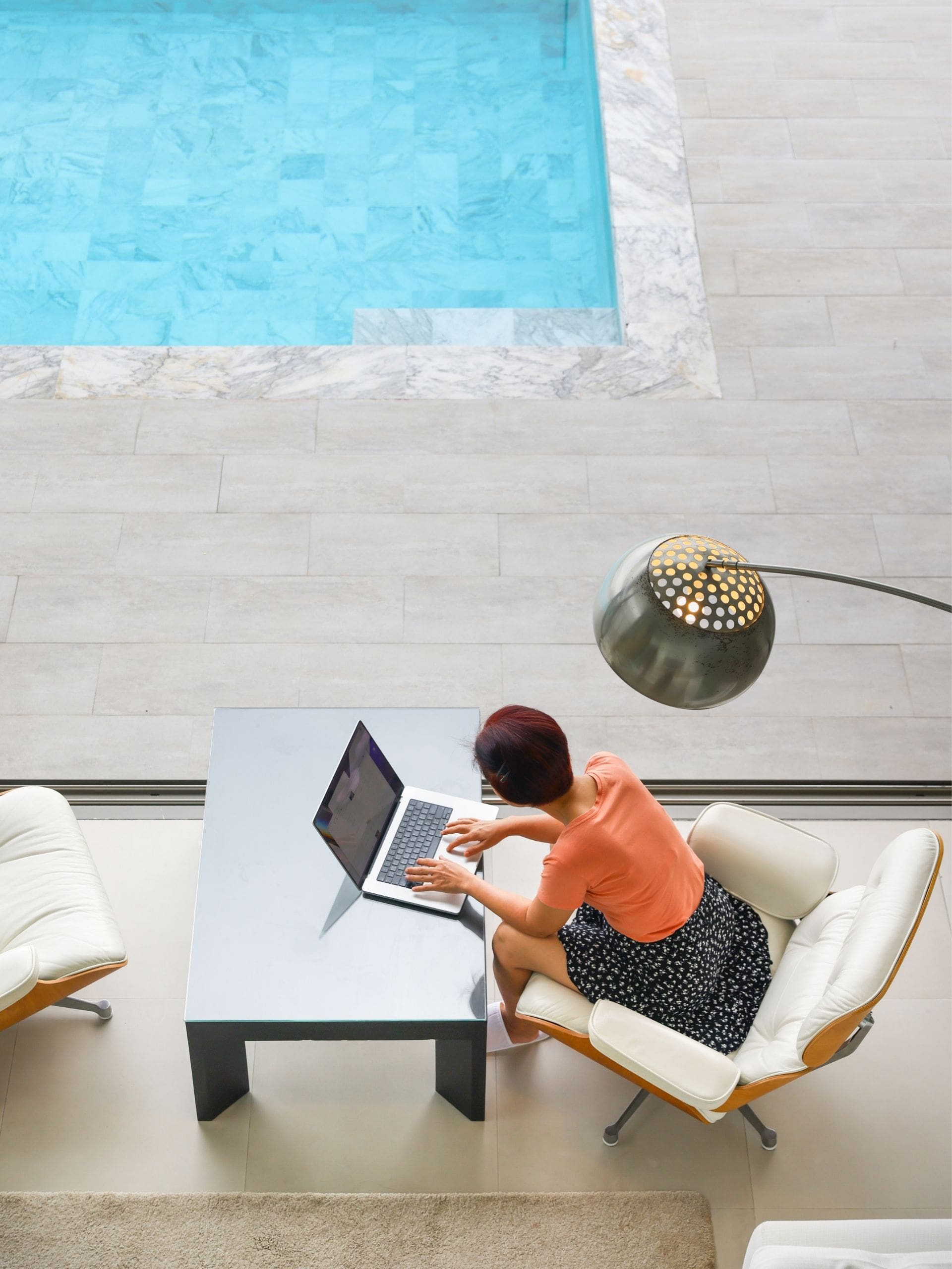 Frau sitzt mit ihrem Laptop am Pool als Symbol für krankenversicherung ausland