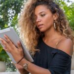 Eine Frau mit lockigen Haaren sitzt im Freien vor ihrem Tablet