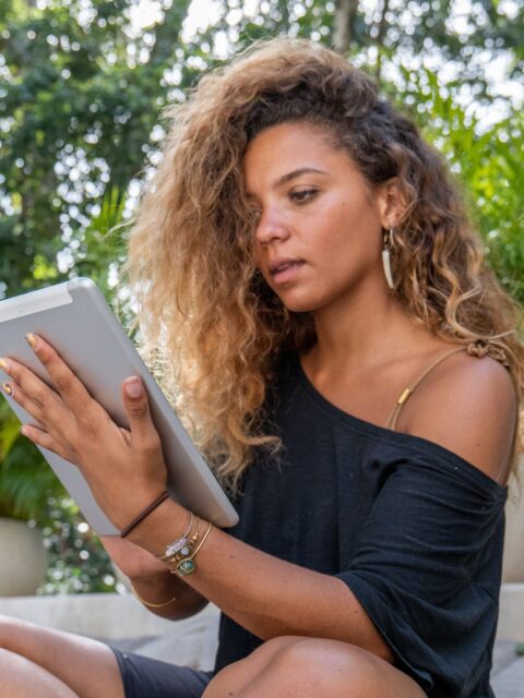 Eine Frau mit lockigen Haaren sitzt im Freien vor ihrem Tablet