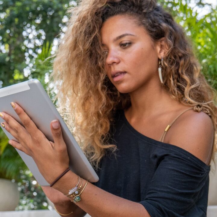 Eine Frau mit lockigen Haaren sitzt im Freien vor ihrem Tablet