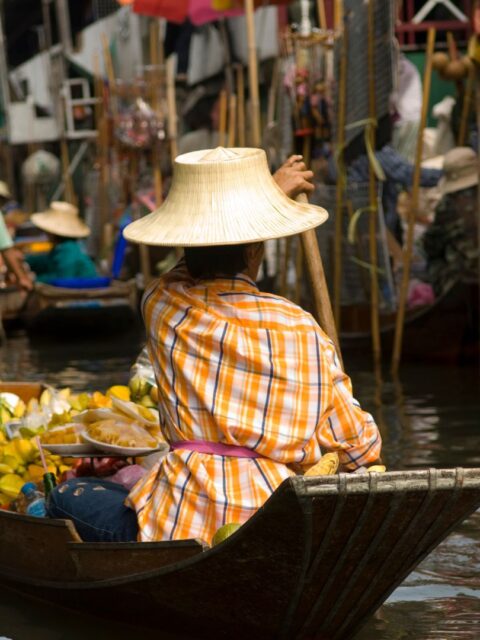 Eine Frau sitzt in ihrem Boot und fährt durch einen thailändischen Markt