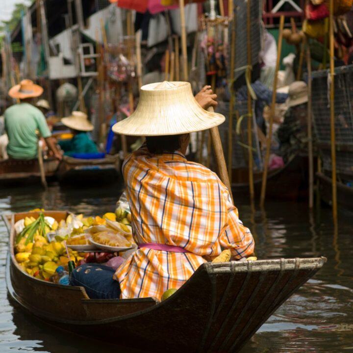 Eine Frau sitzt in ihrem Boot und fährt durch einen thailändischen Markt